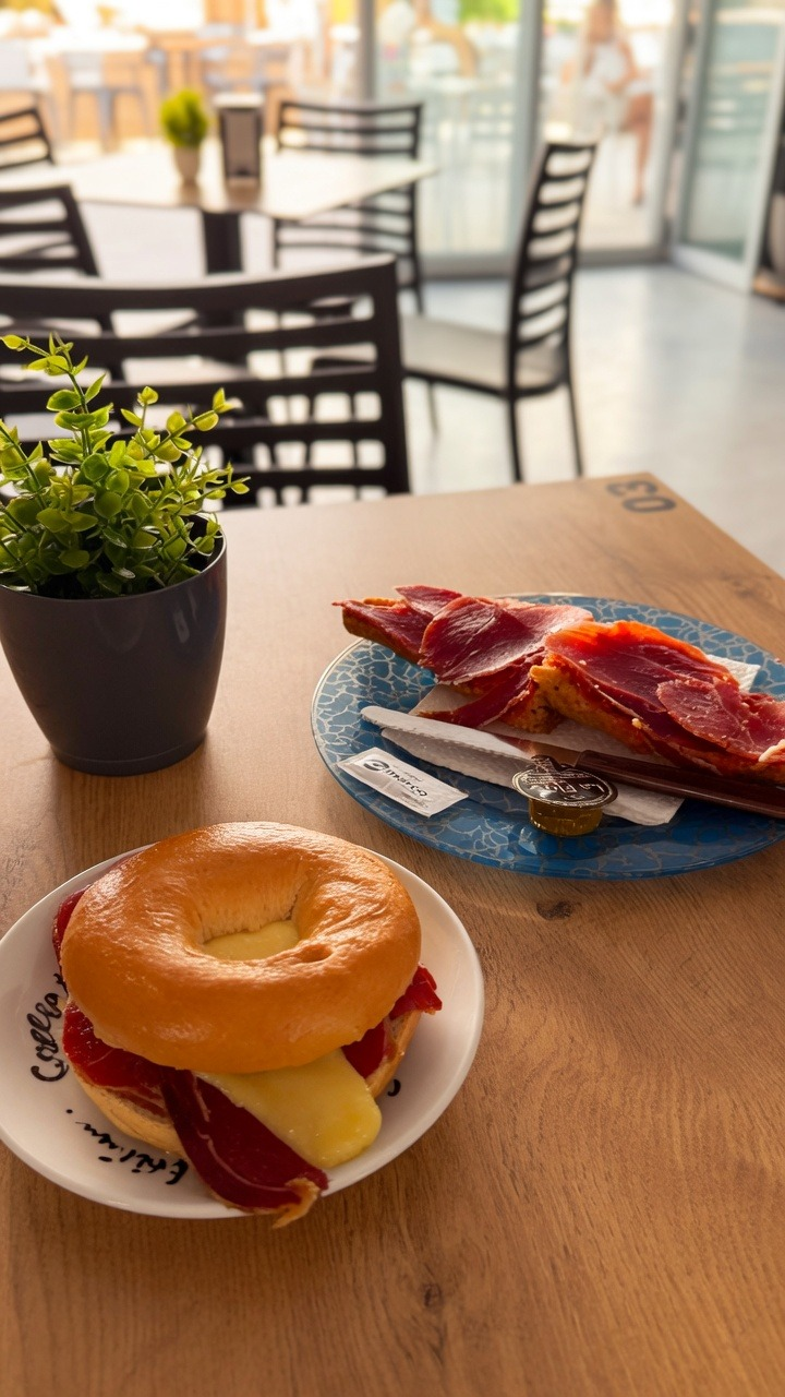Bagel con jamón serrano y queso junto a tabla de jamón
